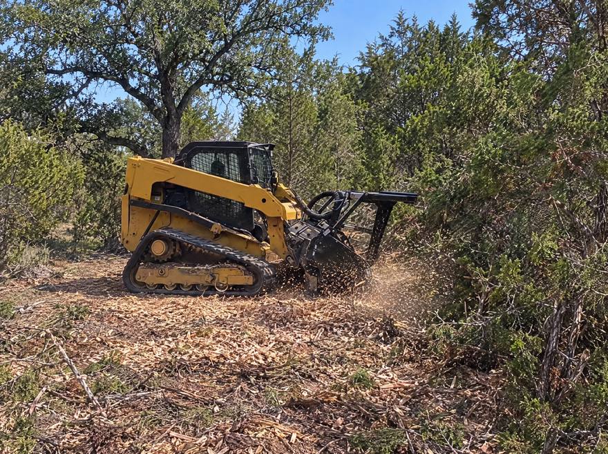A tracked skid steer mulching a cedar tree down to chips